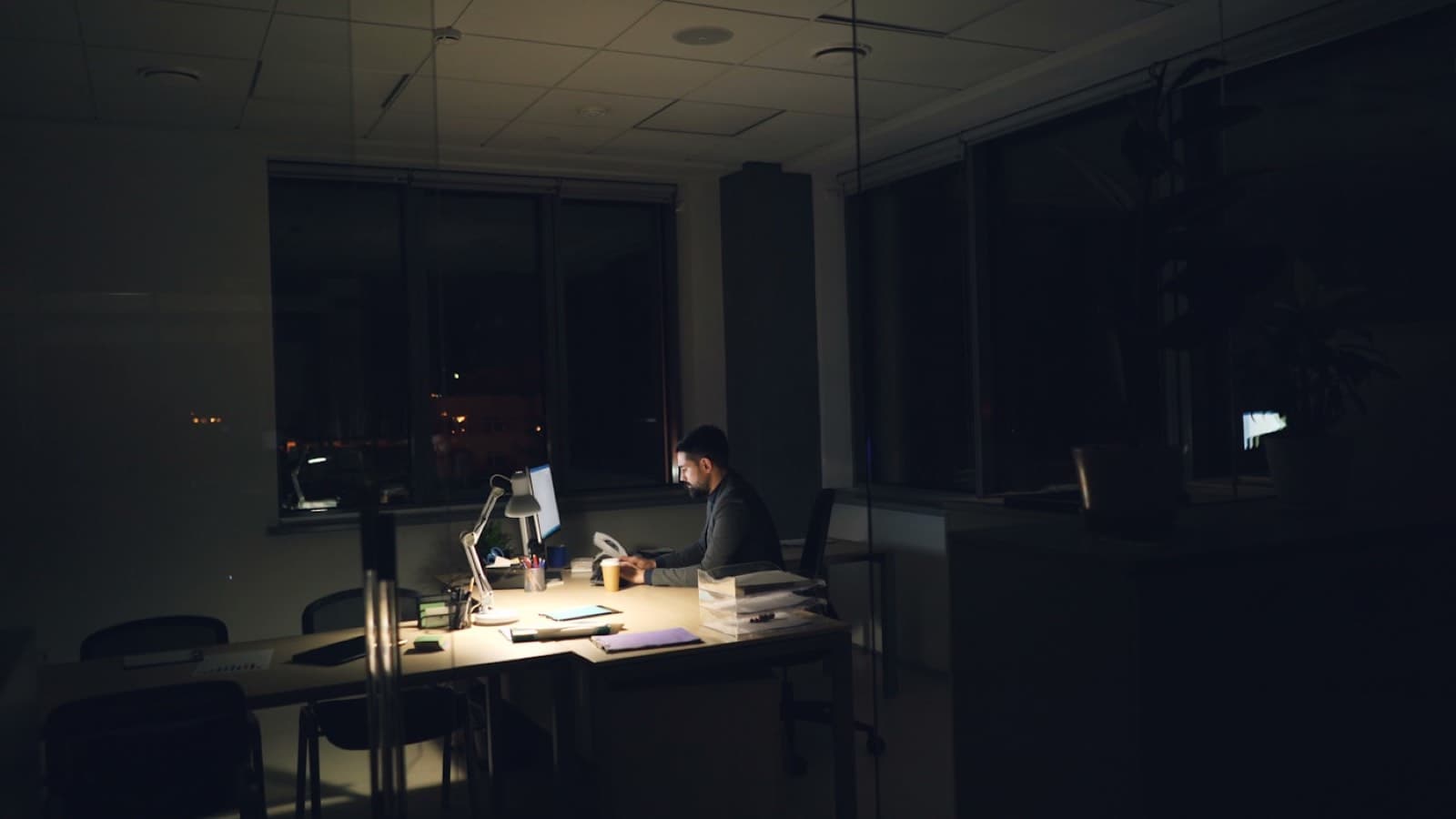 An operator working alone at a lamp-lit desk in a dark office at night