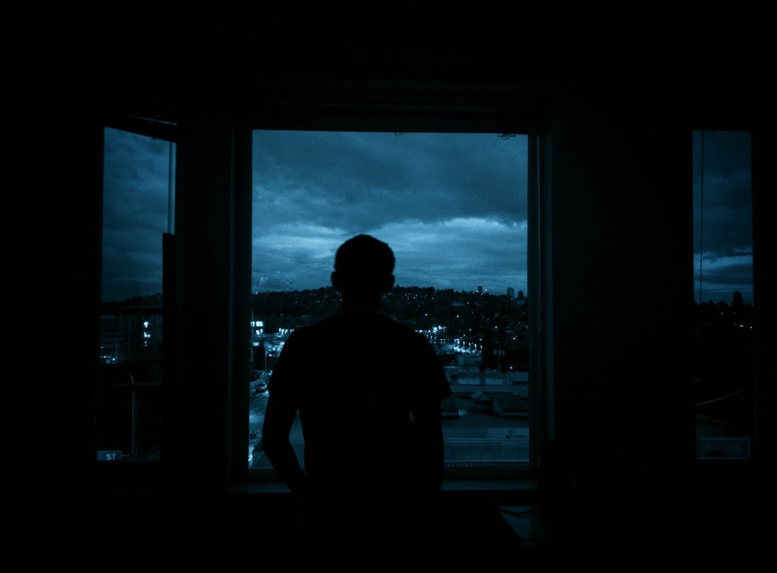 A figure at a window above a city at dusk